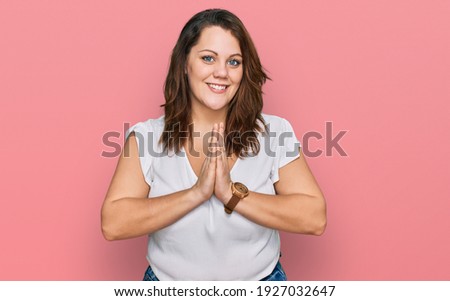 Young plus size woman wearing casual white t shirt praying with hands together asking for forgiveness smiling confident. 