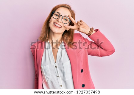Young caucasian woman wearing business style and glasses doing peace symbol with fingers over face, smiling cheerful showing victory 