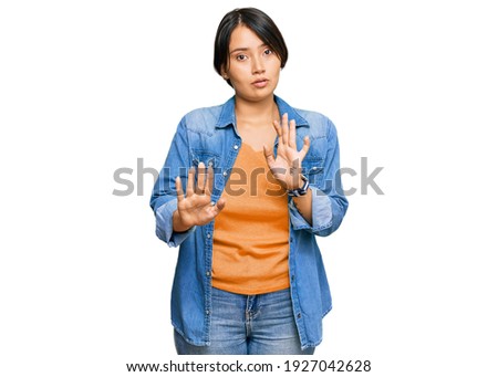 Young beautiful hispanic woman with short hair wearing casual denim jacket moving away hands palms showing refusal and denial with afraid and disgusting expression. stop and forbidden. 