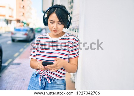 Young latin girl with serious expression using smartphone and headphones at the city