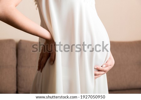 Pregnant woman hold back pain on sofa at thr home. Maternity healthcare concept support products.