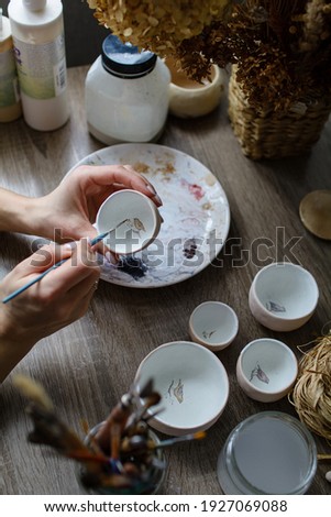 The process of hand-painting a ceramic hand-made bowl. Emphasis on the beautiful female hands of the artist.