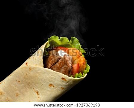Classic tortilla wrap roll with grilled beef, cheese and vegetables, tomato, lettuce with steam smoke on black background