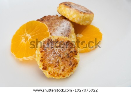 Three sweet curd cottage cheese pancake sprinkled with powdered sugar with two orange slices close-up on a white plate with the ability to copy the space. Concept of a delicious, healthy breakfast