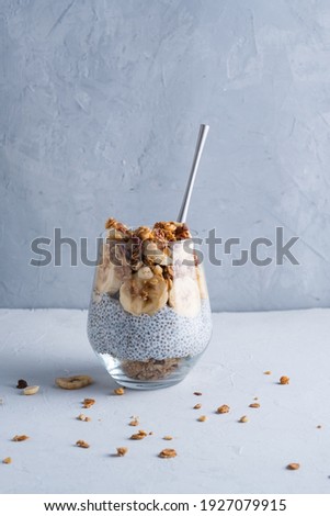 Healthy breakfast in a glass with banana, walnut, chio seeds, yogurt and muesli on a gray background with copy space.