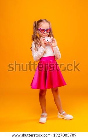 a little girl in sunglasses holds a photo camera on a yellow background
