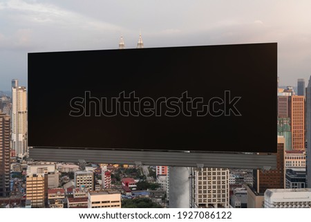 Blank black road billboard with Kuala Lumpur cityscape background at sunset. Street advertising poster, mock up, 3D rendering. Front view.