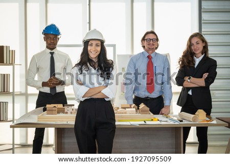 Portrait of smiling businesswoman engineer wearing helmet and diversity team colleague with architect construction model and blueprint.