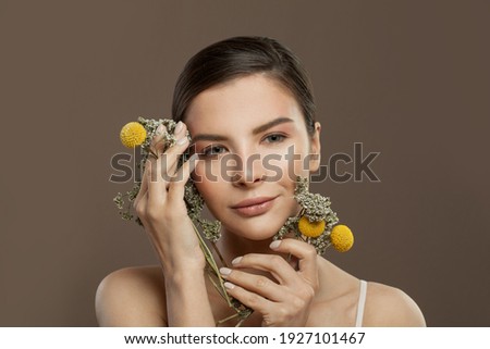 Cheerful woman with clear skin and flowers on brown background. Herbal medicine and skincare concept
