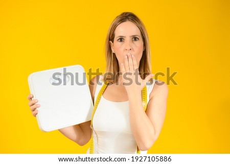 Beautiful surprised woman with scales over yellow background