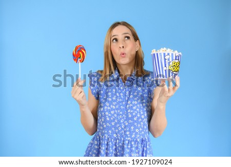 Image of happy cute young woman standing isolated over blue background eating pop corn and lollipop