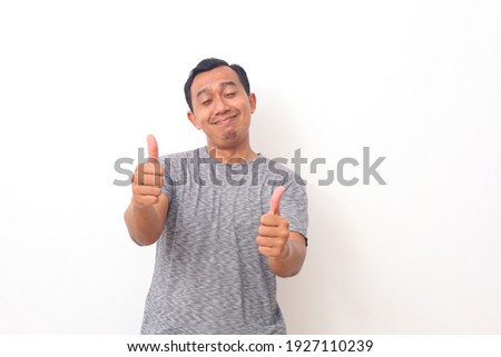 Portrait of Asian man stand happy and positive with thumbs up approving with a big smile and funny face expressing okay gesture isolated over white background