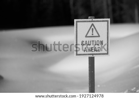 warning caution ahead sign in black and white before frozen pond thin ice in winter with sunny warmer weather fresh 
white snow horizontal format room for type