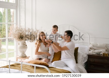Beautiful young family man woman and son in white clothes play on the bed with a rabbit at home