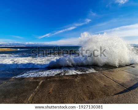 View of big waves crushing on concrete beach during high winds against blue sky Royalty-Free Stock Photo #1927130381