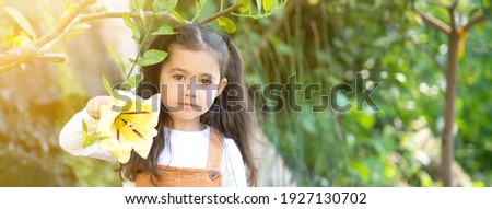 Beautiful child holding a tropical yellow flower on green nature outdoor background. Spring, summer family holiday concept. Mother's day.