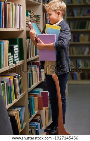school boy taking books from shelves in library, with a stack of books in hands. child brain development, learn to read, cognitive skills concept