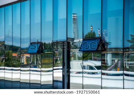 Large windows in a building reflecting the chimneys of a nearby industry