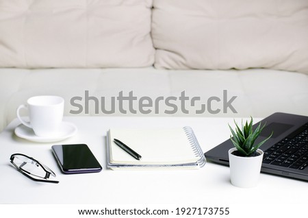 Comfortable workplace at home. Laptop, smartphone, notepad and coffee on table near the sofa