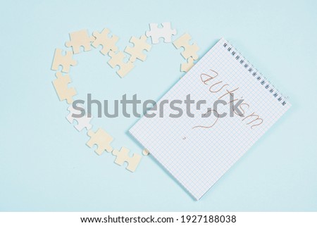 notepad with the inscription autism and wooden puzzle pieces are laid out in the shape of a heart on a light blue background copy space