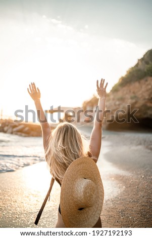 Young beautiful woman in a black swimsuit and hat with glasses walks along the beach in Turkey at sunset. The concept of sea recreation. Selective focus