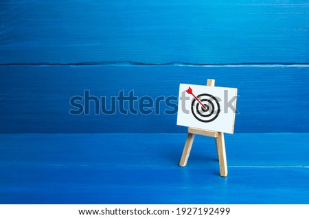 Easel with an arrow in target center. Direct hit, Bulls-eye, straight to the point. Marketing and targeting audience. Complete success. Advertising strategy. Excellent job. Reached goal, best result. Royalty-Free Stock Photo #1927192499