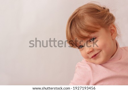little beautiful girl fooling around. Girl on a white background. A happy little girl with light tails, wearing light pink golf. An oily child with blue eyes.