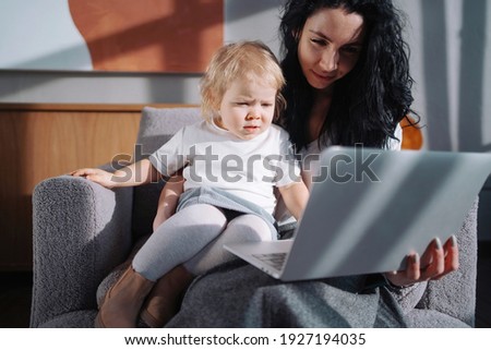 Mom and Blonde Girl watching a cartoon. Children's channel on a laptop, computer. The child in the chair is resting and having a good time. Comfortable children's clothing.