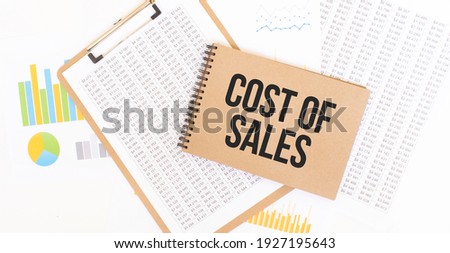 Text COST OF SALES on brown paper notepad on the table with diagram. Business concept