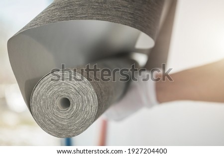 Caucasian Interior Remodeling Worker with Roll of Modern Vinyl Wallpaper Preparing For Wallcover Installation. Royalty-Free Stock Photo #1927204400