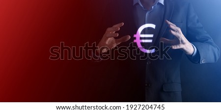 Businessman holds money coin icons EUR or Euro on dark tone background..Growing money concept for business investment and finance.