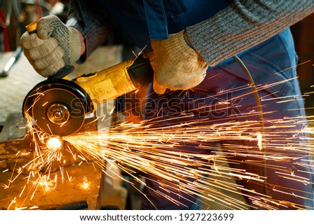 Locksmith in special clothes and goggles works in production. Metal processing with angle grinder. Sparks in metalworking. Royalty-Free Stock Photo #1927223699