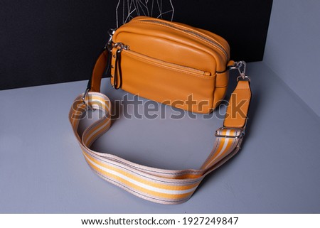 Women's yellow bag with a wide textile belt. Cross body made of artificial leather. Gray and black background. Royalty-Free Stock Photo #1927249847