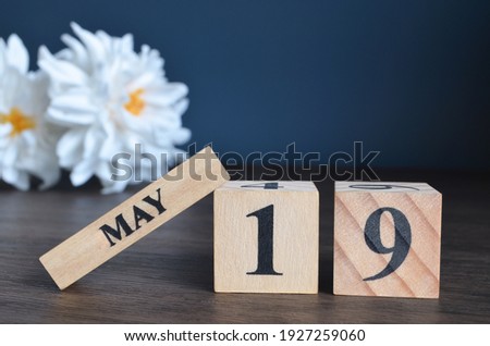 May 19, Date cover design with calendar cube and white Paeonia flower on wooden table and blue background.