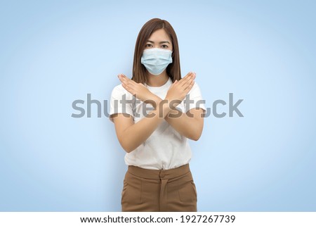 Asian woman wearing face mask protects filter dust pm2.5 anti-pollution, anti-smog, and air pollution her crossed arms show X sign isolated on blue background. with copy space and clipping paths.