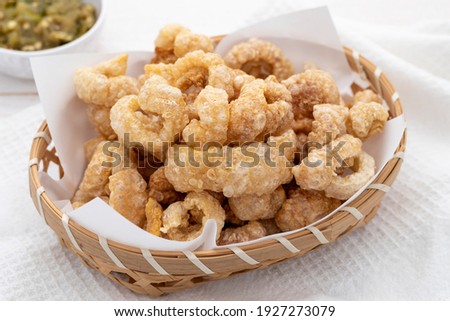 Perfect pork scratchings or pork cracklings served in a bamboo basket together with hot green chili dip. It is a popular Thai food dish from northern Thailand. Royalty-Free Stock Photo #1927273079