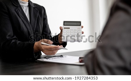A car rental company employee holds a white calculator to show the tenant the rental price, the employee calculates the cost of the car rental before entering into the lease agreement with the renter. Royalty-Free Stock Photo #1927284353