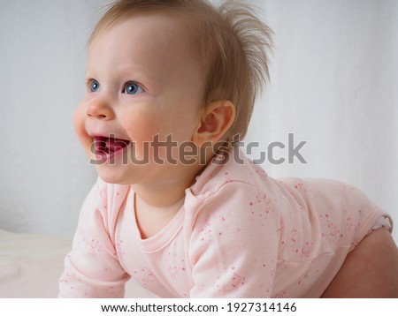 Cute gentle baby girl, 10 months old, bright blue eyes, crawling, laughing merrily, close-up. Portrait of a girl in pink tones. Baby products concept. Real children's emotions. Royalty-Free Stock Photo #1927314146