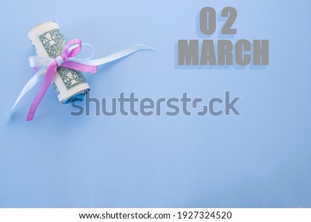 calendar date on blue background with rolled up dollar bills pinned by blue and pink ribbon with copy space.  March 2 is the second  day of the mont.