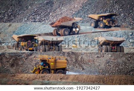 Six trucks in a busy modern gold mine in Western Australia. One water truck and five large haul truck transport gold ore from the Super Pit, Opencast mine. All logos removed Royalty-Free Stock Photo #1927342427