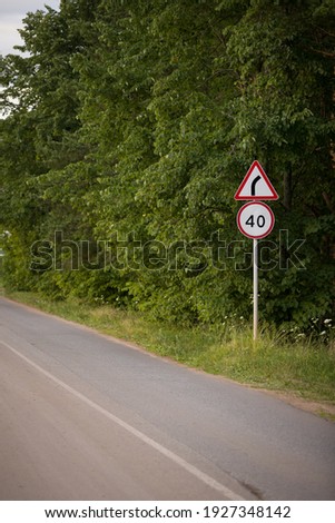 Road sign - speed limit 40 km h and sign - attention, dangerous turn. Road signs on the road against the background of a green forest.