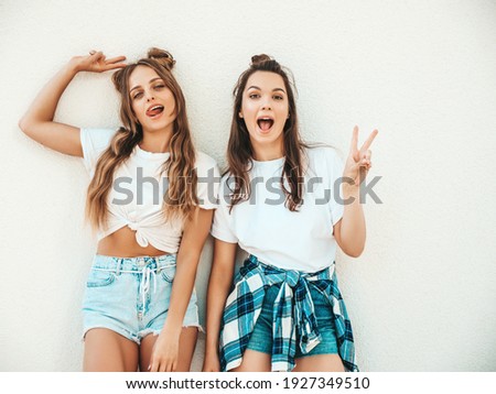 Portrait of two young beautiful smiling hipster women in trendy summer white t-shirt clothes.Sexy carefree women posing on street background. Positive models having fun, hugging and going crazy Royalty-Free Stock Photo #1927349510
