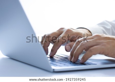 Hands of a man with white shirt typing on a laptop or notebook computer on a desktop while working in the office using internet, input data for information analysis and sending an email message. Royalty-Free Stock Photo #1927359245