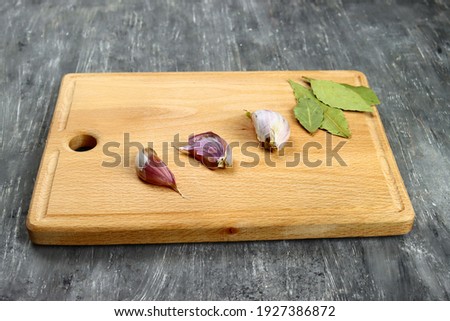 Wooden cutting board with garlic and bay leaves on a gray table