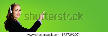 Call Center Service. Customer support or sales agent. Businesswoman or caller or phone operator in black suit showing pointing at copy space or imaginary. Green background. Help answering, consulting.