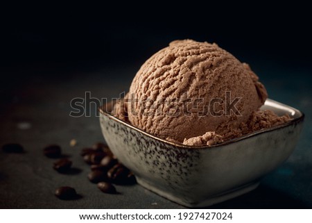 Scoop of tasty chocolate gelato with creamy texture in square shaped bowl on table with aromatic roasted coffee beans on dark background