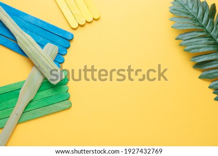 Spatula on a blue and green and yellow wood stick and green tropical leaves palm put on a yellow background with copy space. Minimal summer background concept. Flat lay.
