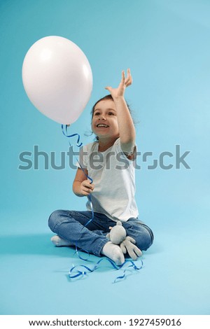 Beautiful little girl playing with a pink balloon in her hand expressing happiness. Concept of Children Protection Day. Blue background with copy space