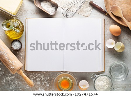 Baking and Cooking Ingredients Flour Eggs Rolling Pin Butter And blank recipe book Background. Top View Copy Space Royalty-Free Stock Photo #1927471574