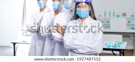 The team of scientists wear white clothing and two layers of protective equipment, a medical mask and 1 layer Transparent model in the science room

